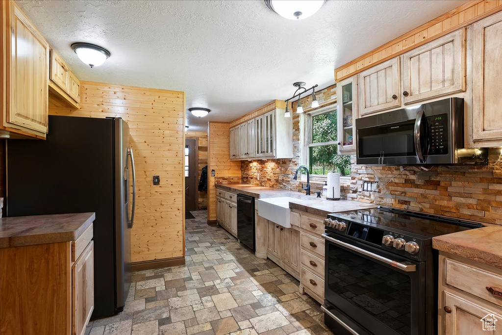 Kitchen featuring black appliances, decorative backsplash, glass insert cabinets, light stone finish floors, and a textured ceiling