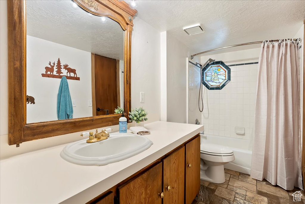 Full bath featuring stone tile flooring, a textured ceiling, vanity, and shower / bath combo with shower curtain