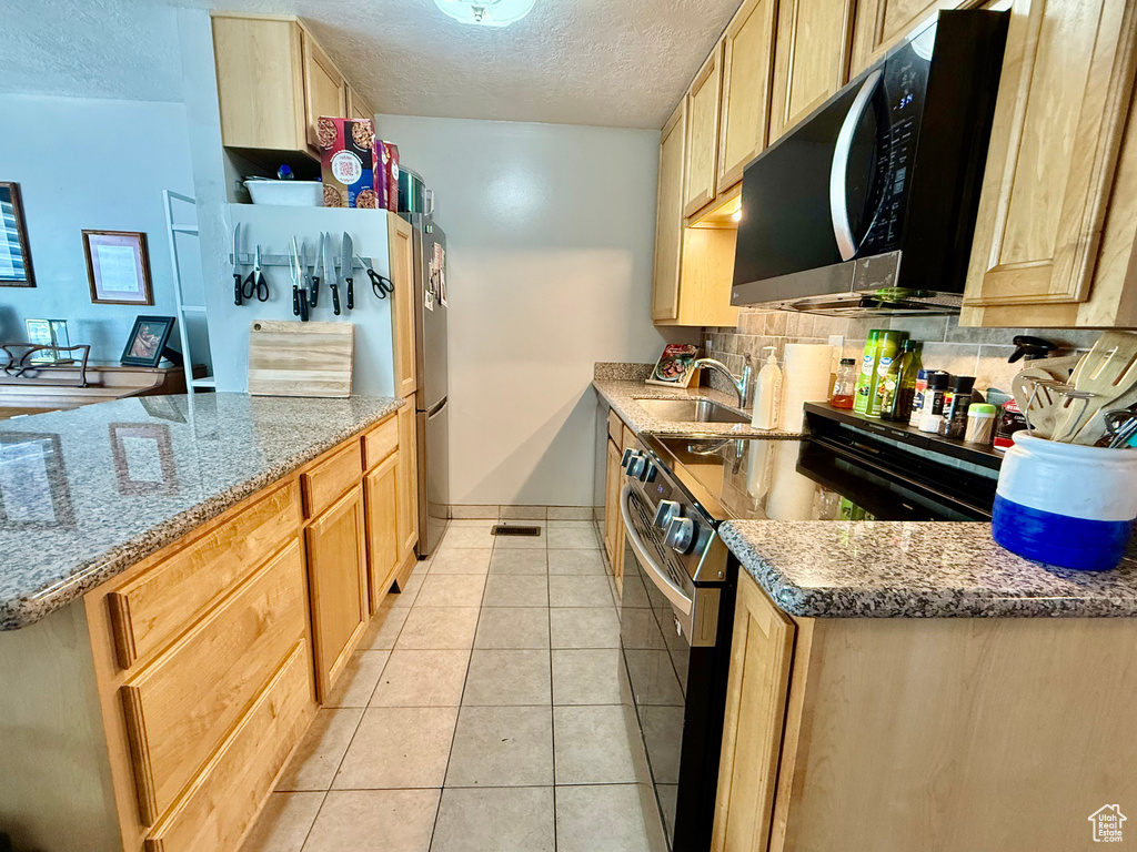 Kitchen featuring appliances with stainless steel finishes, a textured ceiling, light brown cabinets, tasteful backsplash, and light tile patterned floors