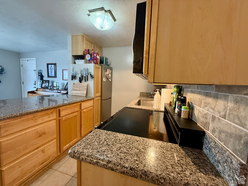 Kitchen featuring freestanding refrigerator, a textured ceiling, dark stone countertops, a peninsula, and light tile patterned floors