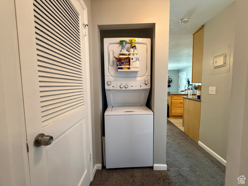 Laundry room with stacked washer / drying machine, dark carpet, and a textured ceiling