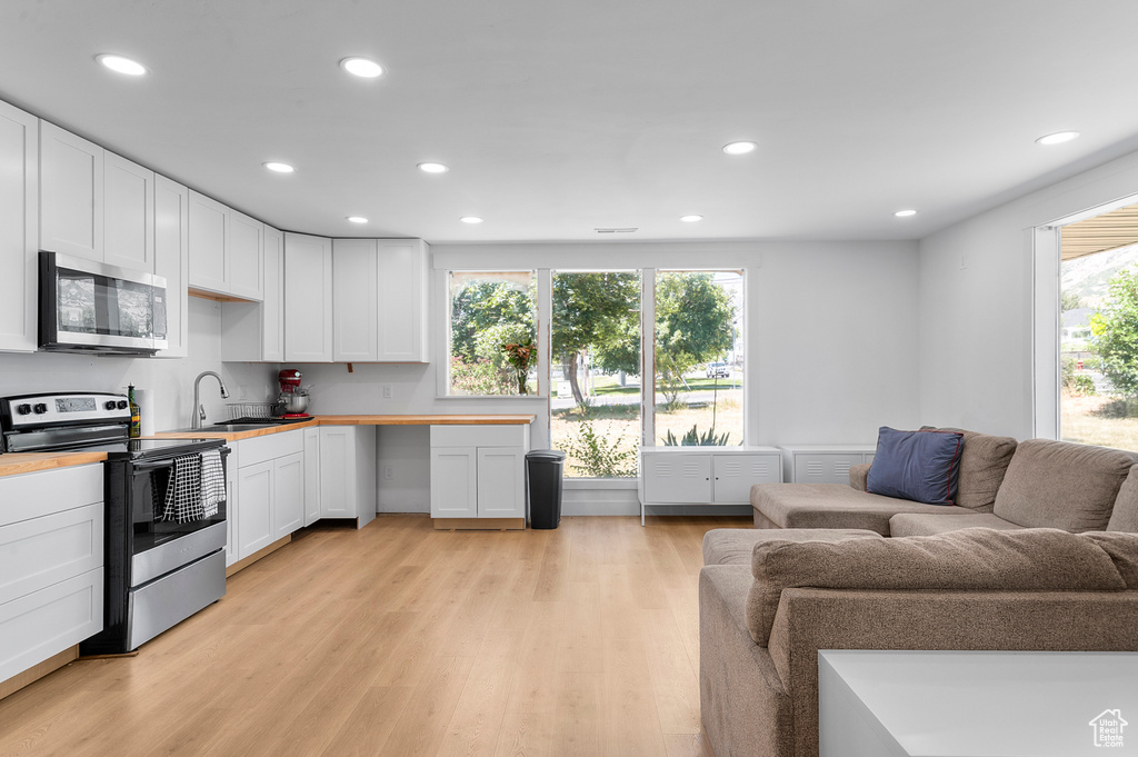 Kitchen featuring appliances with stainless steel finishes, white cabinetry, recessed lighting, light wood finished floors, and wood counters