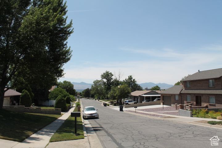 View of asphalt road featuring sidewalks, a mountain view, and curbs