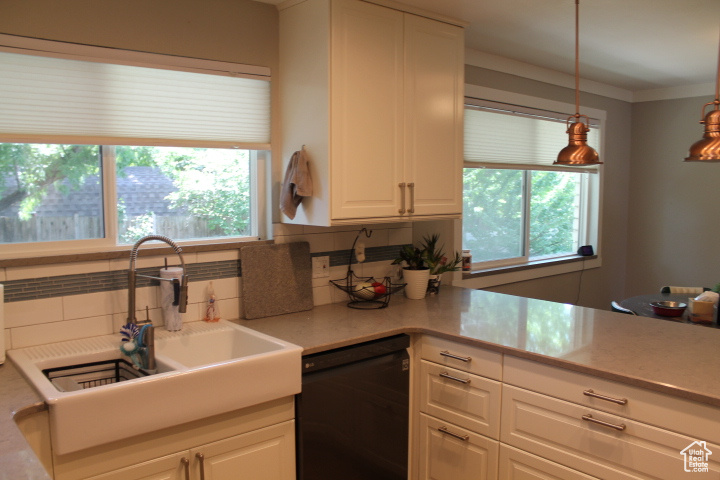 Kitchen featuring black dishwasher, tasteful backsplash, white cabinetry, light countertops, and hanging light fixtures