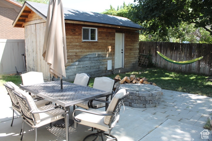 Fenced backyard with an outdoor fire pit, a patio, an outbuilding, and outdoor dining space