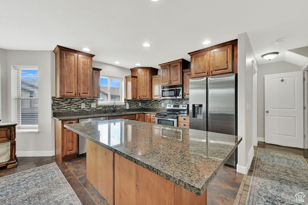 Kitchen featuring appliances with stainless steel finishes, backsplash, a kitchen island, dark stone countertops, and recessed lighting
