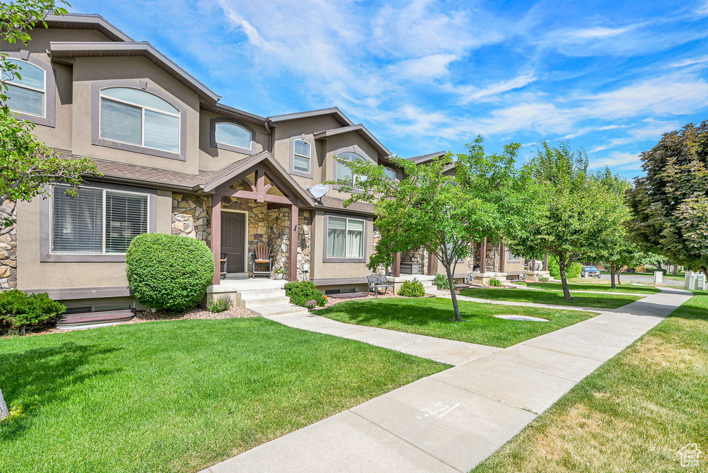View of property featuring stucco siding, stone siding, and a front yard