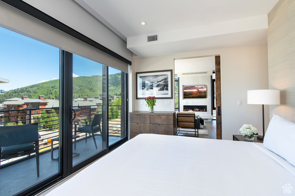 Bedroom with a warm lit fireplace, access to exterior, and a mountain view