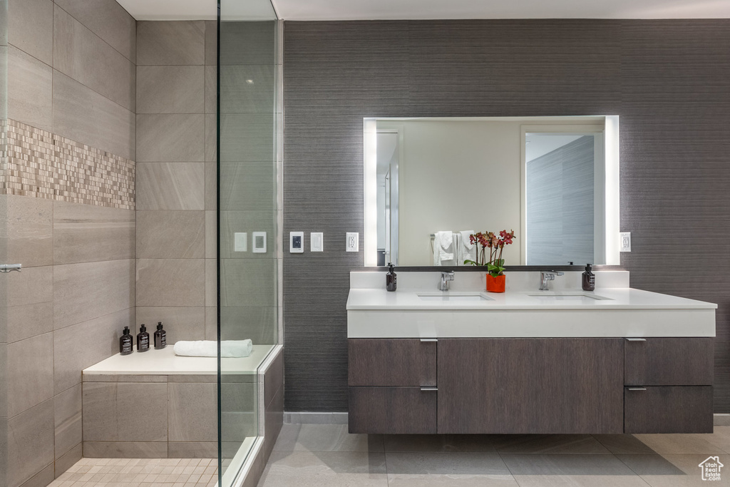 Bathroom featuring double vanity, tile patterned floors, and tiled shower
