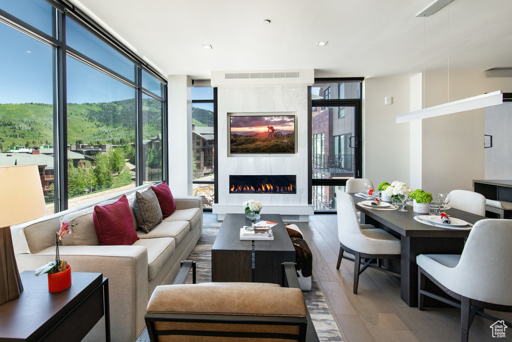 Living area featuring a wall of windows, hardwood / wood-style flooring, healthy amount of natural light, and a warm lit fireplace