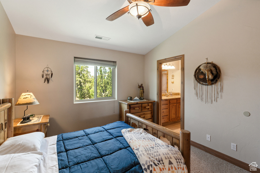 Bedroom featuring light carpet, vaulted ceiling, ceiling fan, and ensuite bathroom