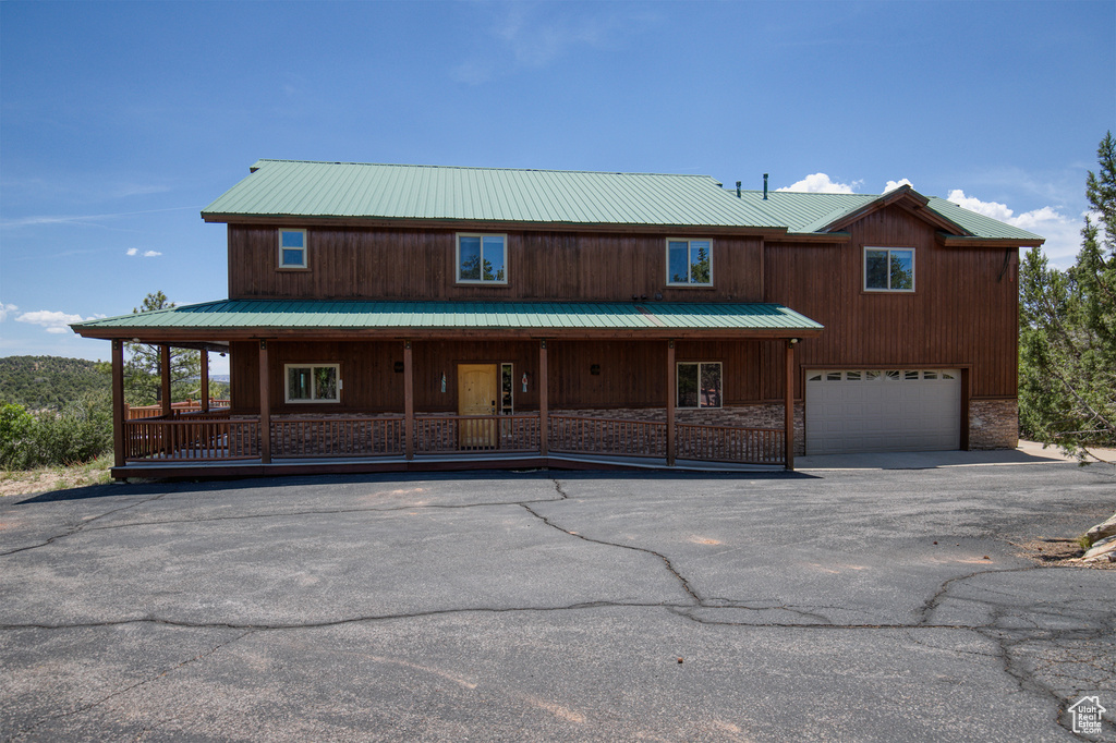 View of front of house with covered porch, a metal roof, stone siding, an attached garage, and asphalt driveway