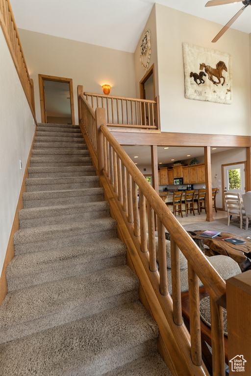 Stairway with carpet, ceiling fan, and a towering ceiling