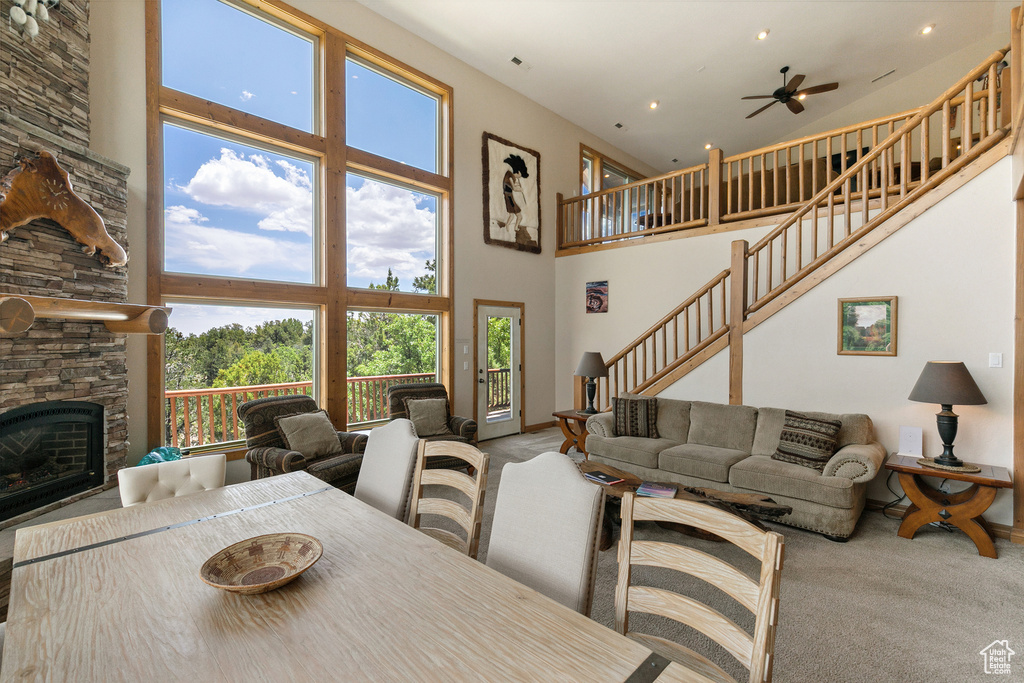 Carpeted dining area featuring a high ceiling, a ceiling fan, stairs, a fireplace, and recessed lighting