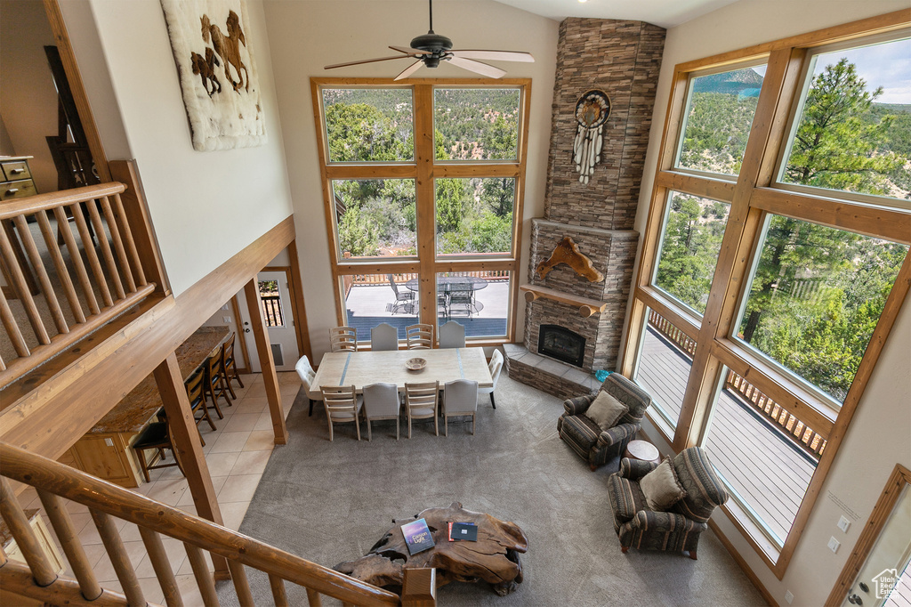 Tiled living room with a ceiling fan, healthy amount of natural light, a stone fireplace, and a high ceiling