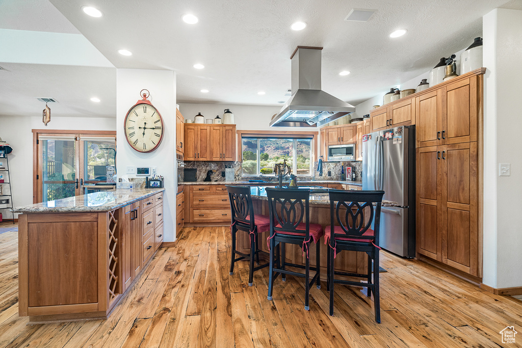 Kitchen with stainless steel appliances, island exhaust hood, light wood-style floors, a peninsula, and a kitchen bar