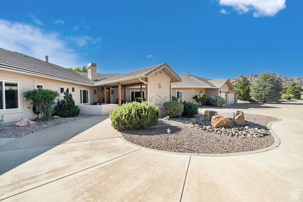 View of front facade featuring stucco siding, a garage, a chimney, and concrete driveway