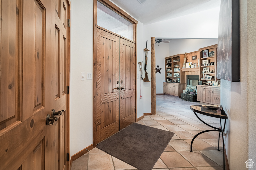 Entryway with a ceiling fan, a fireplace, light tile patterned flooring, and lofted ceiling