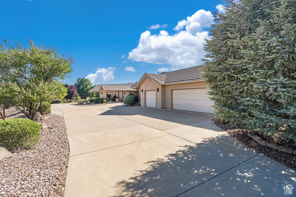 View of front facade featuring concrete driveway, a tiled roof, an attached garage, and stucco siding
