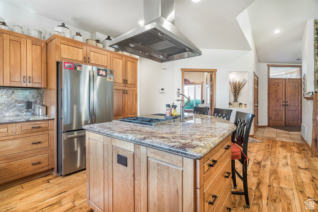 Kitchen with island exhaust hood, stainless steel appliances, a breakfast bar area, light wood-style flooring, and light stone counters