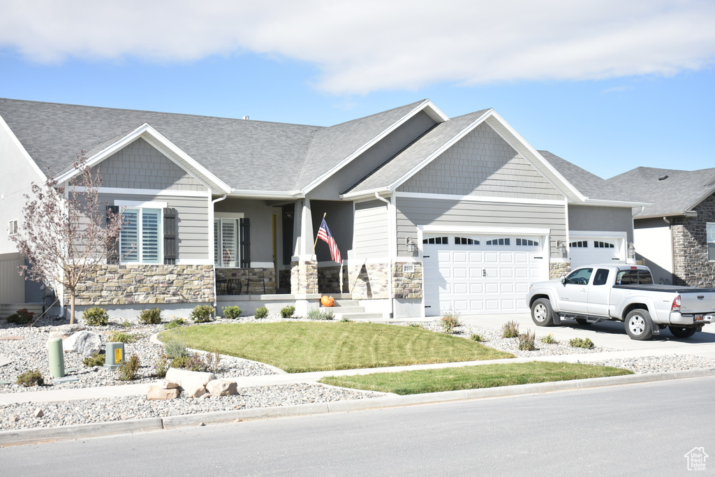 Craftsman-style house with a garage, stone siding, a front yard, and concrete driveway