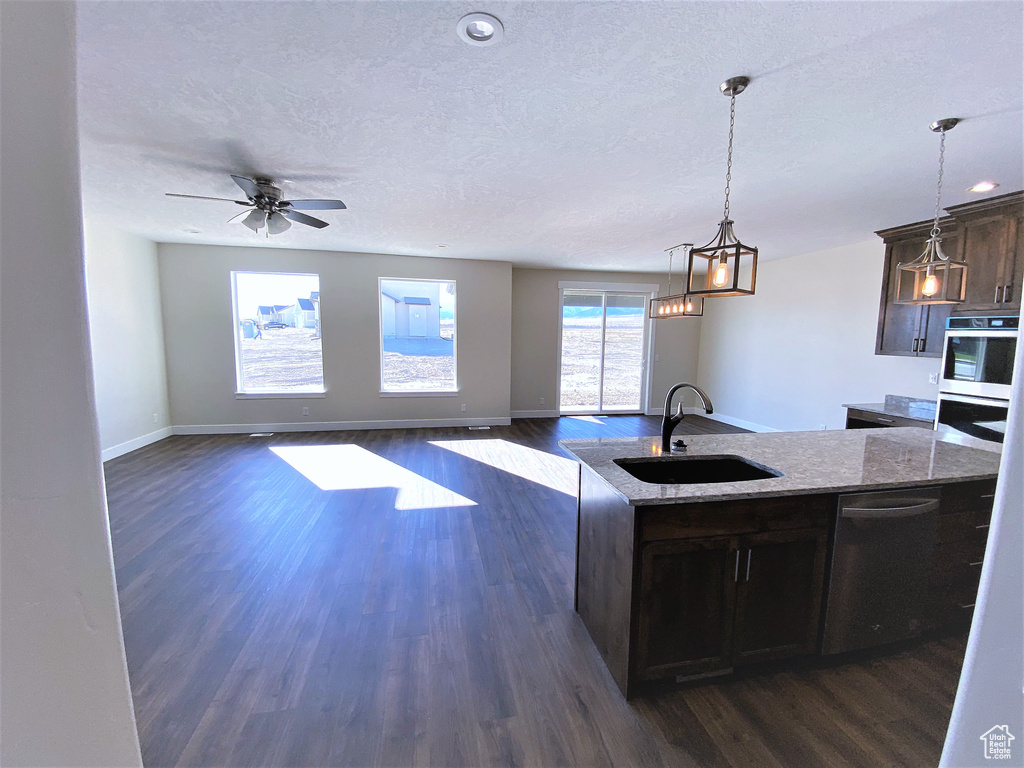 Kitchen featuring stainless steel appliances, dark wood-type flooring, a textured ceiling, light stone countertops, and hanging light fixtures