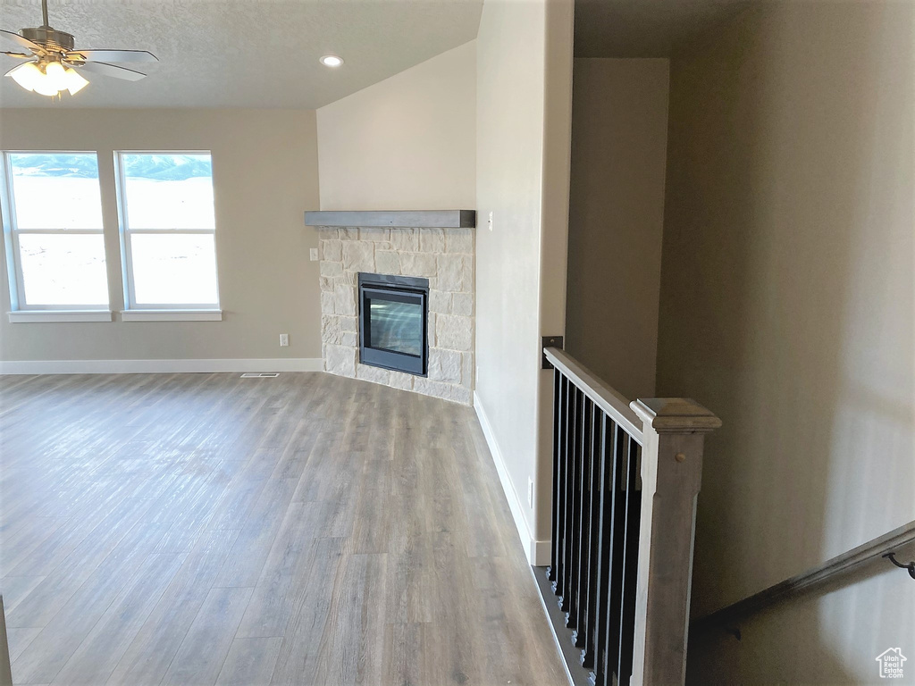 Unfurnished living room featuring wood finished floors, a ceiling fan, a stone fireplace, and recessed lighting