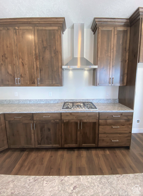 Kitchen featuring wall chimney range hood, stainless steel gas stovetop, dark wood-style floors, dark brown cabinetry, and light stone countertops