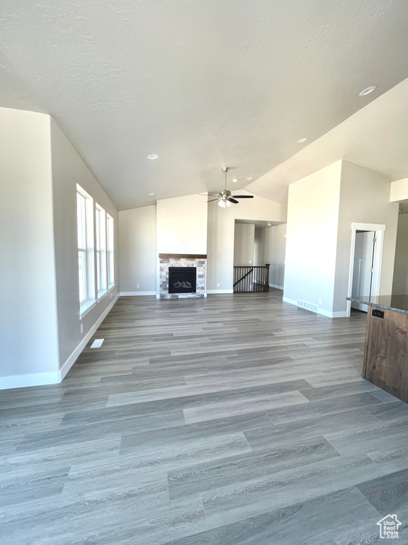 Unfurnished living room with vaulted ceiling, a ceiling fan, a fireplace, light wood-style flooring, and recessed lighting