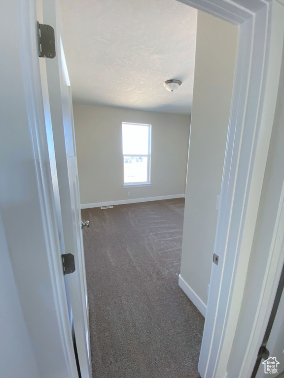 Unfurnished room featuring dark colored carpet and baseboards
