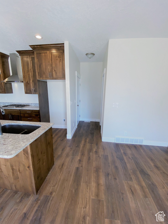 Kitchen featuring wall chimney exhaust hood, gas cooktop, dark wood-style floors, and light stone counters