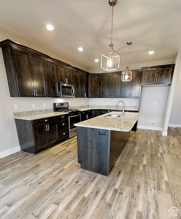 Kitchen with appliances with stainless steel finishes, light wood finished floors, dark brown cabinetry, decorative light fixtures, and recessed lighting