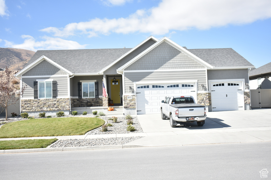Craftsman house featuring an attached garage, stone siding, a front yard, and driveway