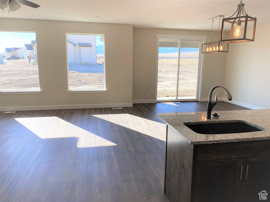 Kitchen with light stone countertops, dark wood-style flooring, pendant lighting, and ceiling fan