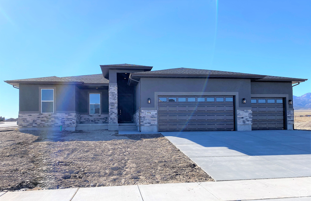 Prairie-style home with stucco siding, a garage, and stone siding
