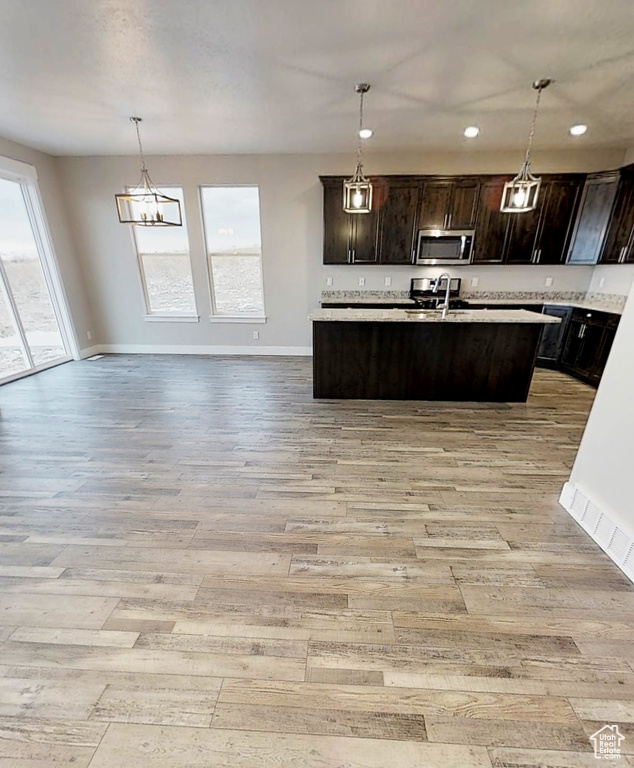 Kitchen with stainless steel microwave, light wood-style flooring, open floor plan, light countertops, and dark brown cabinets