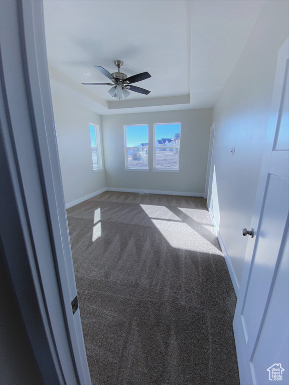 Carpeted spare room featuring a tray ceiling and ceiling fan