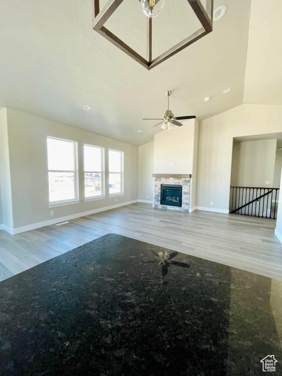 Unfurnished living room featuring wood finished floors, ceiling fan, a textured ceiling, a glass covered fireplace, and lofted ceiling