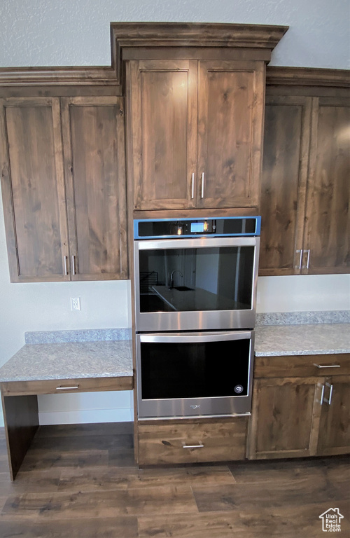 Kitchen view of stainless steel double oven, dark wood-style flooring, light countertops, and dark brown cabinetry