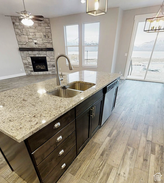 Kitchen with stainless steel dishwasher, light wood-type flooring, pendant lighting, a ceiling fan, and a fireplace