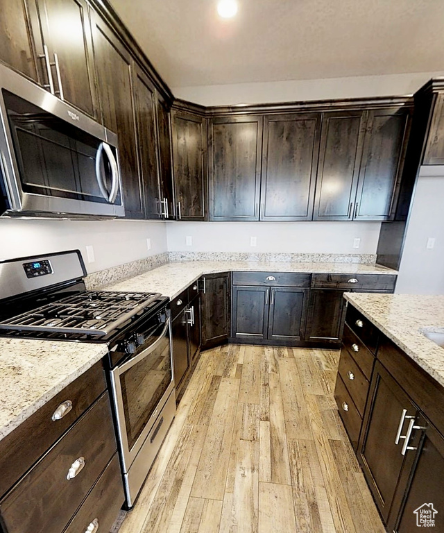 Kitchen with stainless steel appliances, light wood finished floors, light stone countertops, and dark brown cabinets