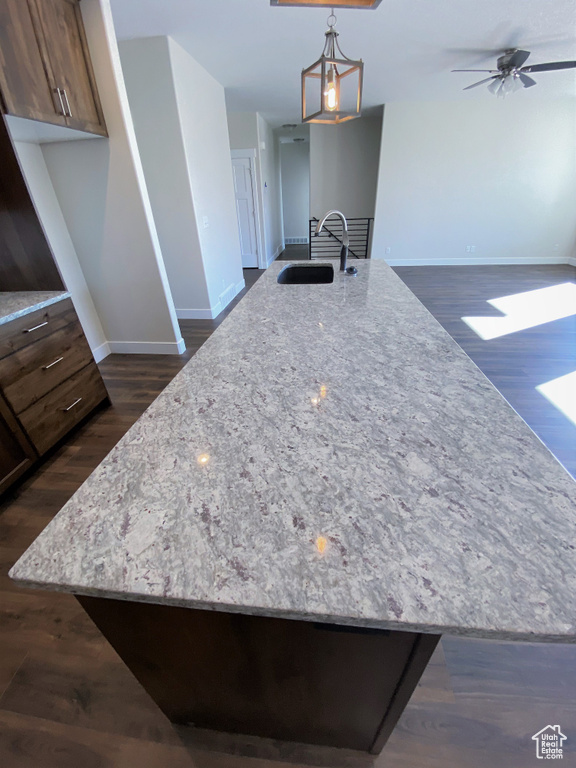 Kitchen with dark wood-style floors, light stone countertops, and a kitchen island with sink