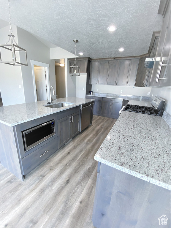 Kitchen with gas range oven, light wood finished floors, a textured ceiling, stainless steel microwave, and light stone counters
