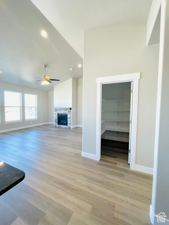 Unfurnished living room with lofted ceiling, ceiling fan, light wood-style floors, a fireplace, and a textured ceiling