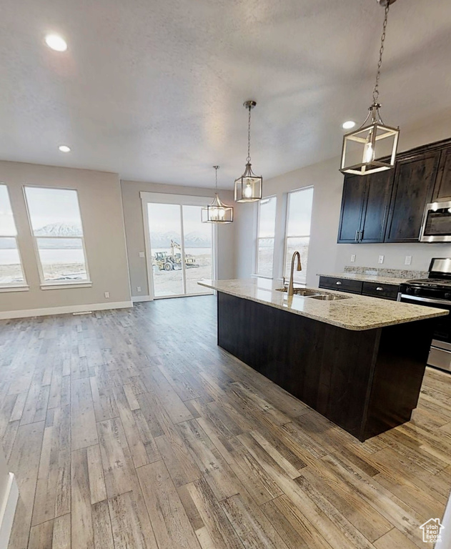 Kitchen featuring stainless steel appliances, light wood finished floors, a kitchen island with sink, recessed lighting, and light stone countertops