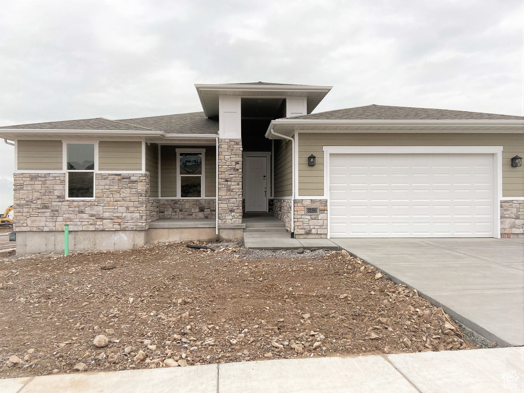 Prairie-style home featuring stone siding, driveway, covered porch, and an attached garage