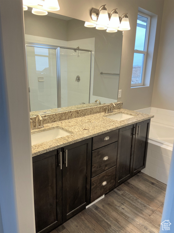 Full bathroom with a stall shower, a bath, double vanity, and wood finished floors