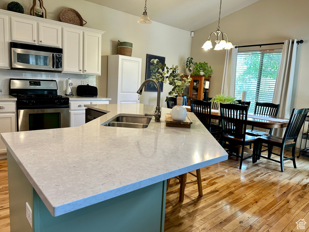 Kitchen with stainless steel appliances, a center island with sink, lofted ceiling, light wood-type flooring, and backsplash