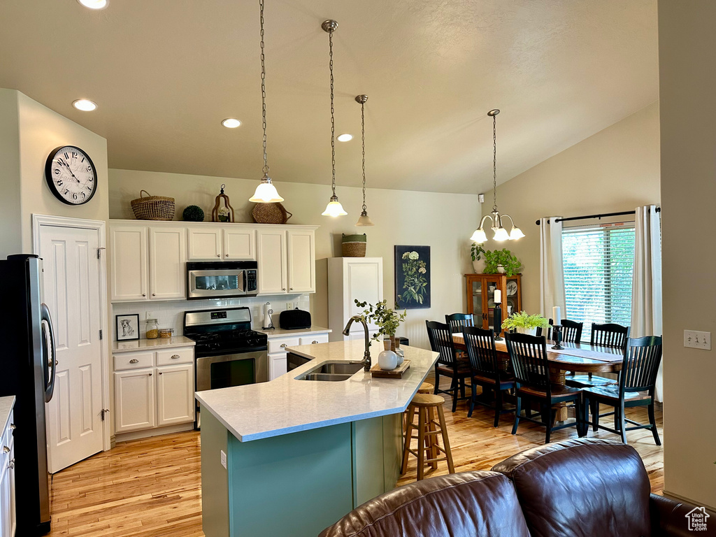 Kitchen featuring appliances with stainless steel finishes, light wood finished floors, a breakfast bar, lofted ceiling, and a chandelier