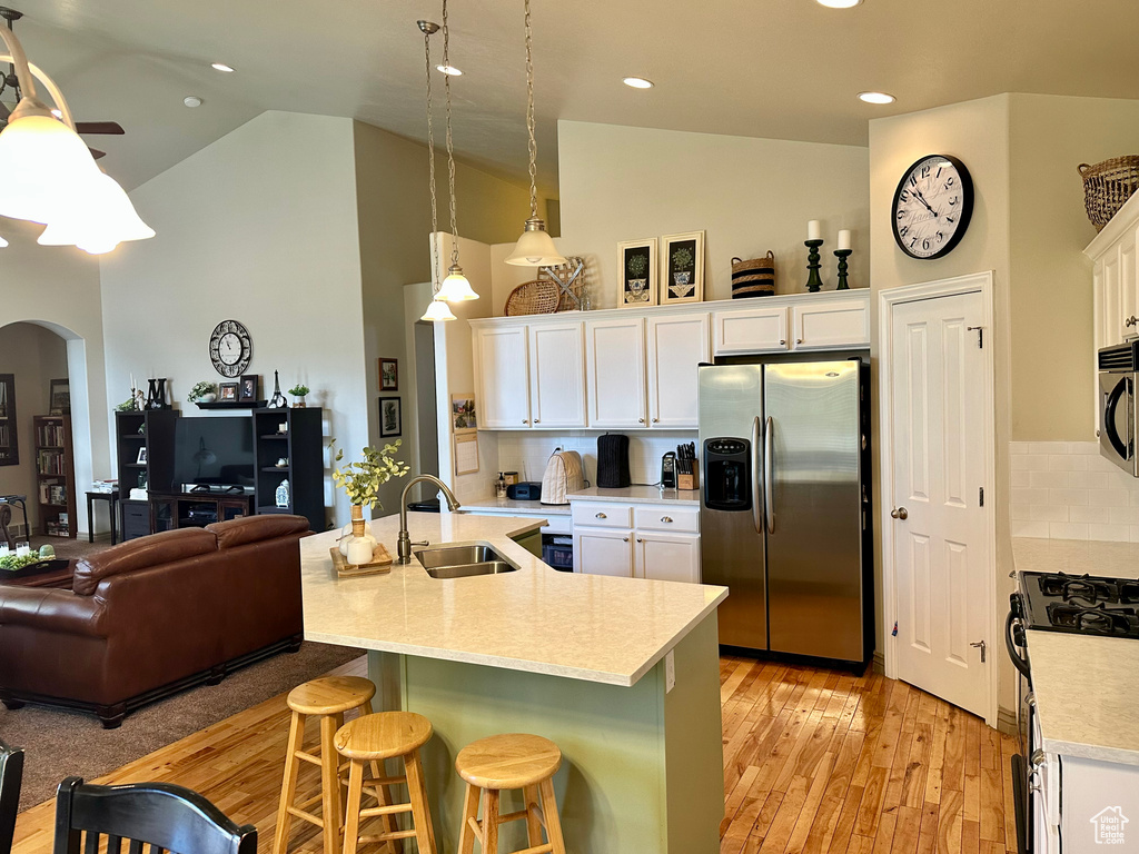 Kitchen featuring appliances with stainless steel finishes, arched walkways, high vaulted ceiling, a breakfast bar area, and white cabinetry